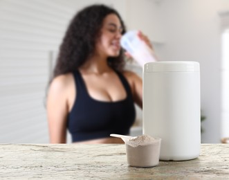 Protein powder on table in room where woman drinking protein shake, selective focus