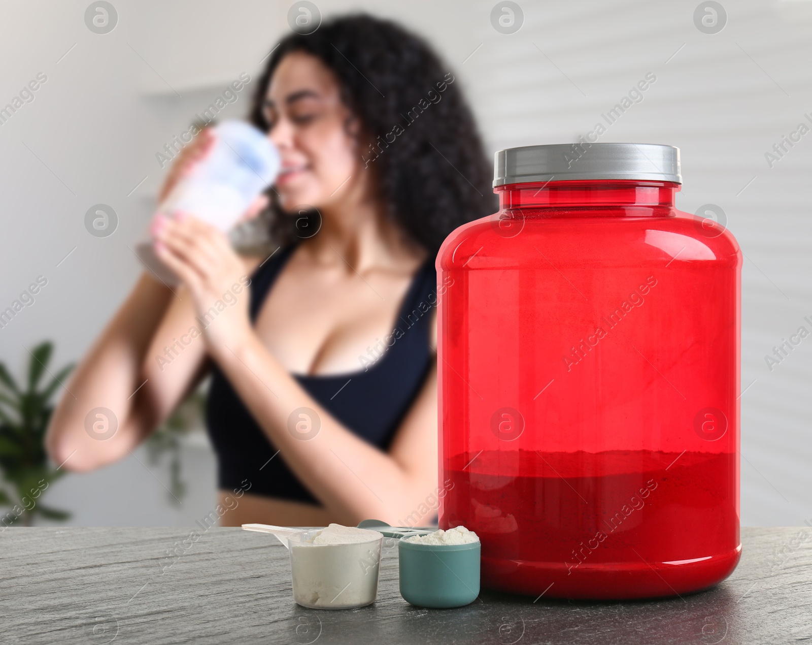 Image of Protein powder on table in room where woman drinking protein shake, selective focus