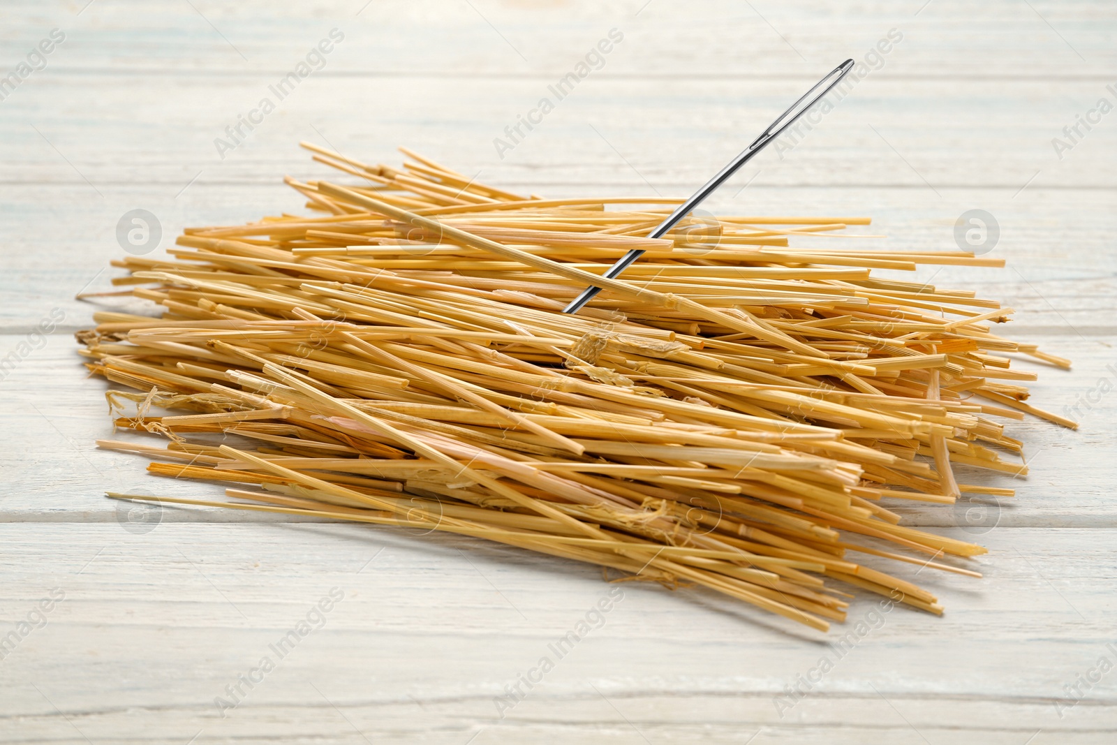 Image of Sewing needle in hay on white wooden background, closeup view