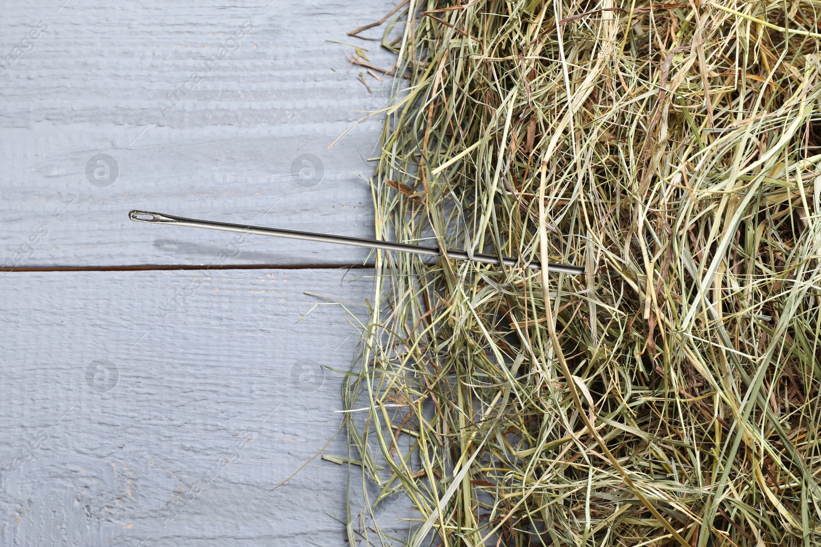 Image of Sewing needle in haystack on grey wooden background, top view