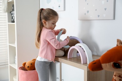 Photo of Little girl playing with toys on chest of drawers indoors