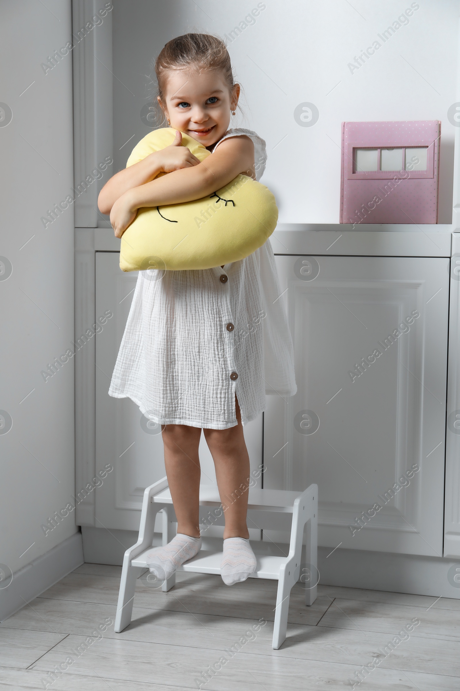 Photo of Little girl with toy standing on step stool indoors