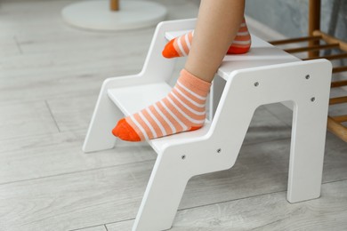 Photo of Little girl standing on step stool indoors, closeup