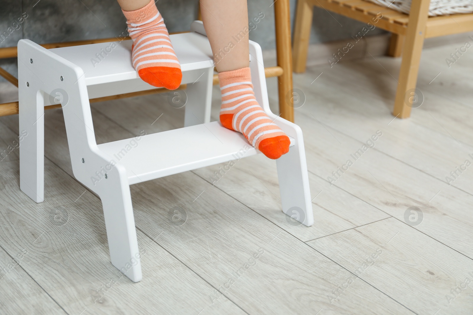 Photo of Little girl standing on step stool indoors, closeup. Space for text