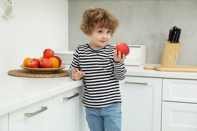 Photo of Little boy with red apple in kitchen