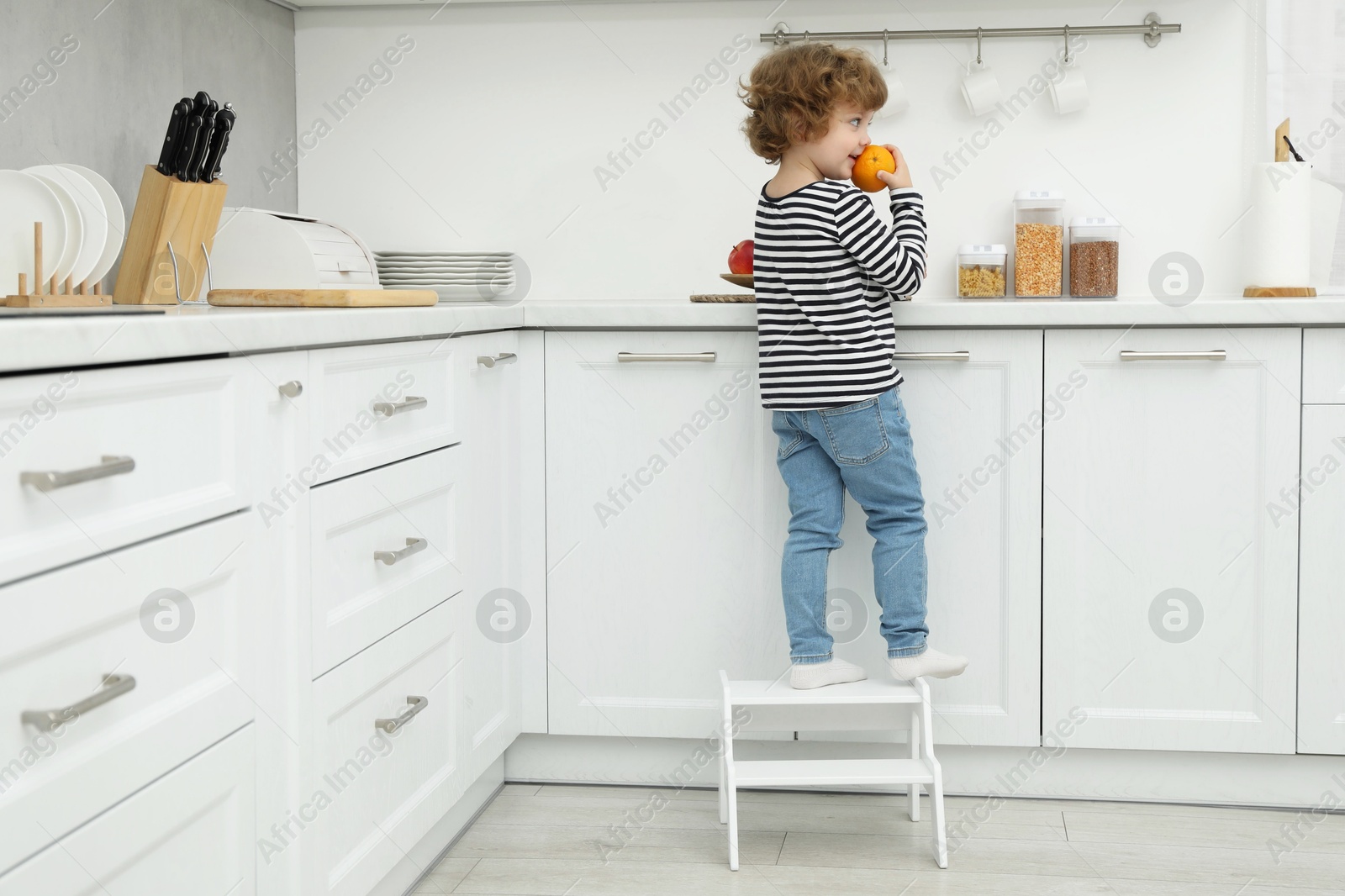 Photo of Little boy with orange standing on step stool in kitchen