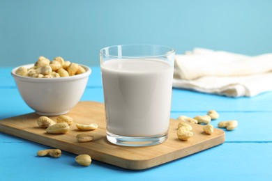 Photo of Fresh cashew milk in glass and nuts on light blue wooden table, closeup