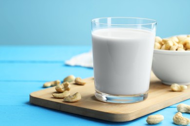 Fresh cashew milk in glass and nuts on light blue wooden table, closeup