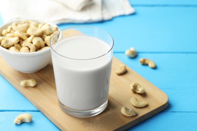 Photo of Fresh cashew milk in glass and nuts on light blue wooden table, closeup