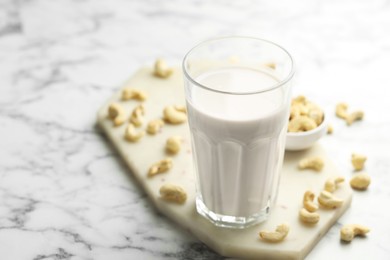 Fresh cashew milk in glass and nuts on white marble table, closeup. Space for text