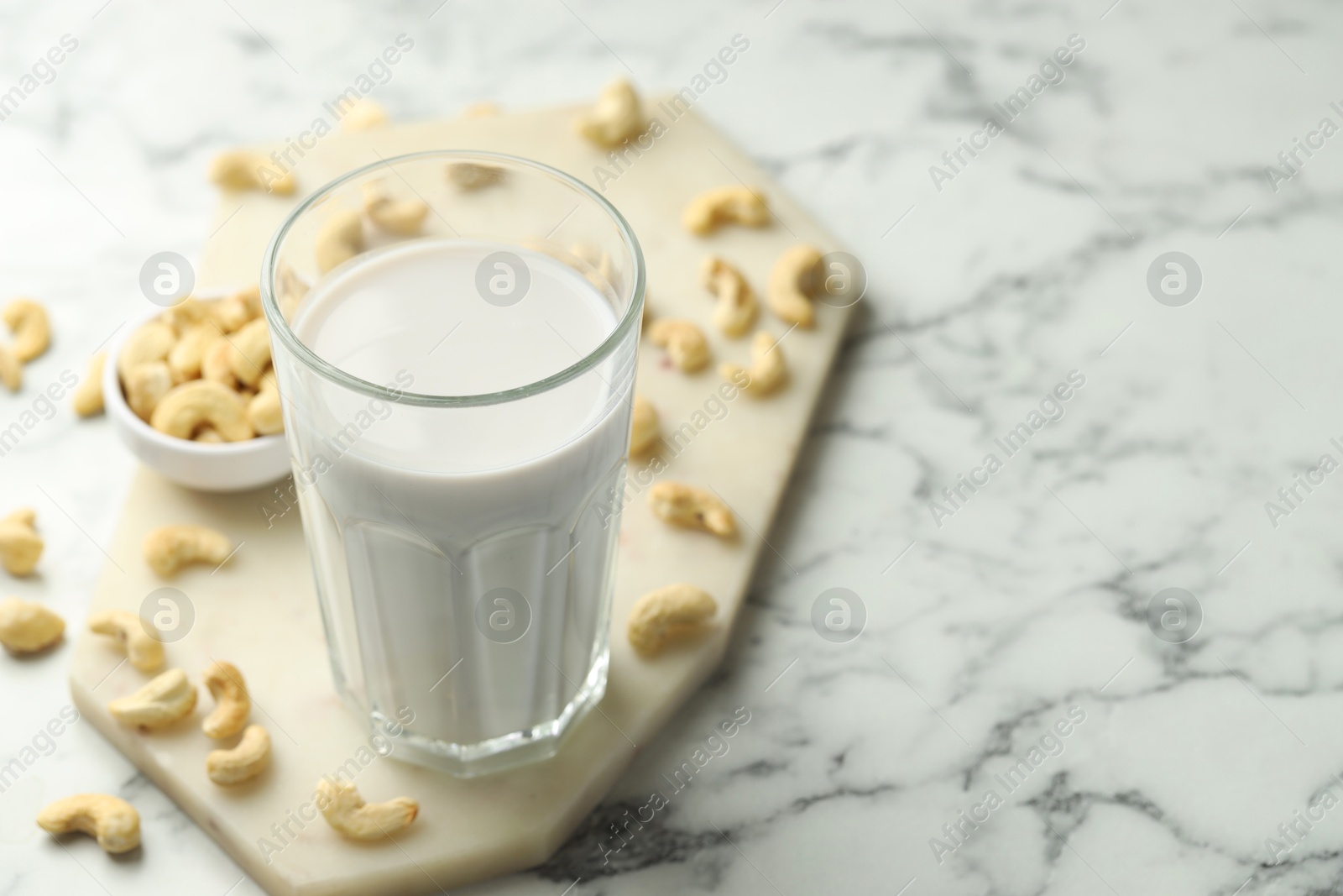 Photo of Fresh cashew milk in glass and nuts on white marble table, closeup. Space for text