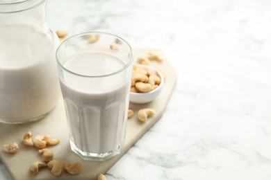 Fresh cashew milk in glass and nuts on white marble table, closeup. Space for text