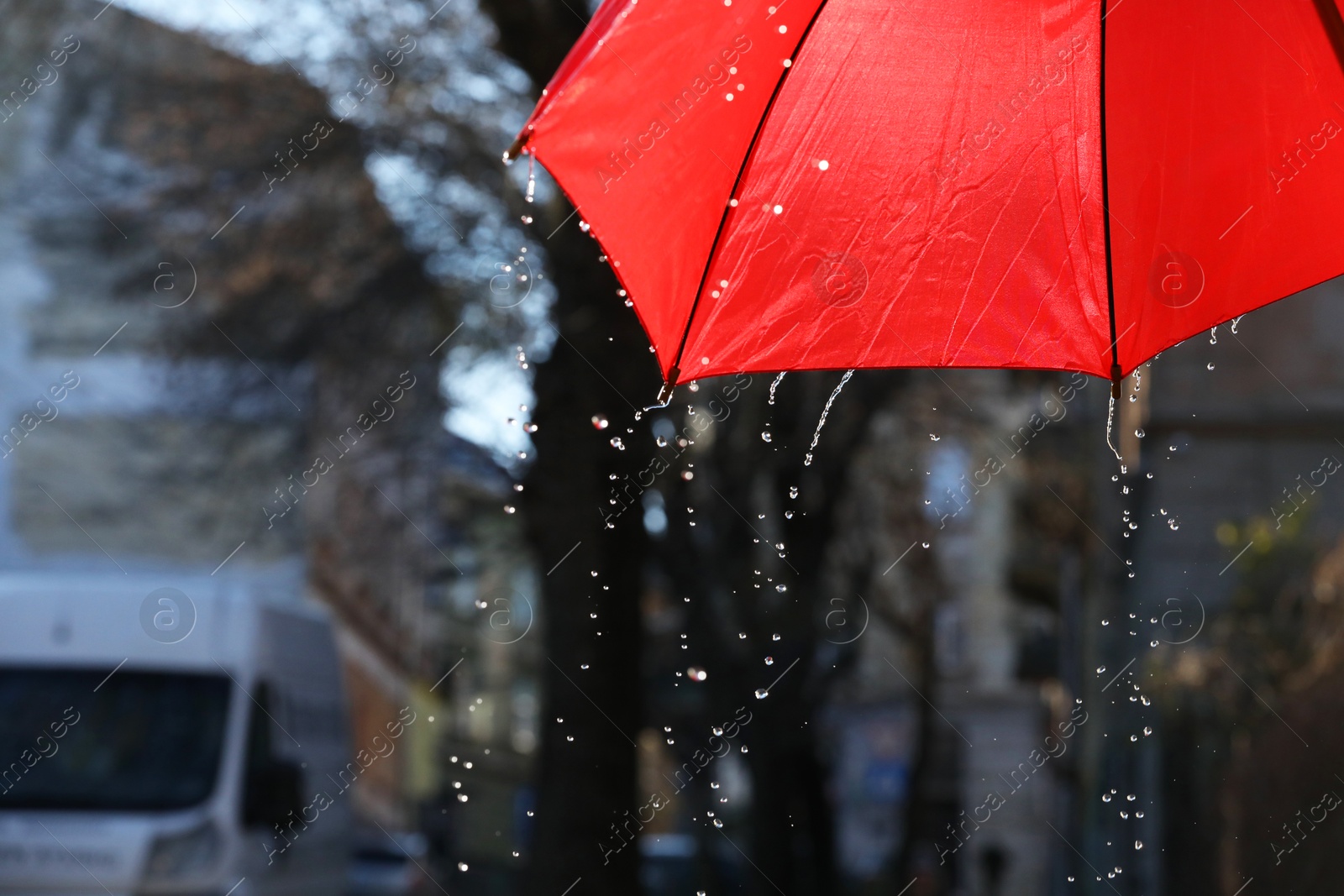 Photo of Open red umbrella under pouring rain outdoors, closeup