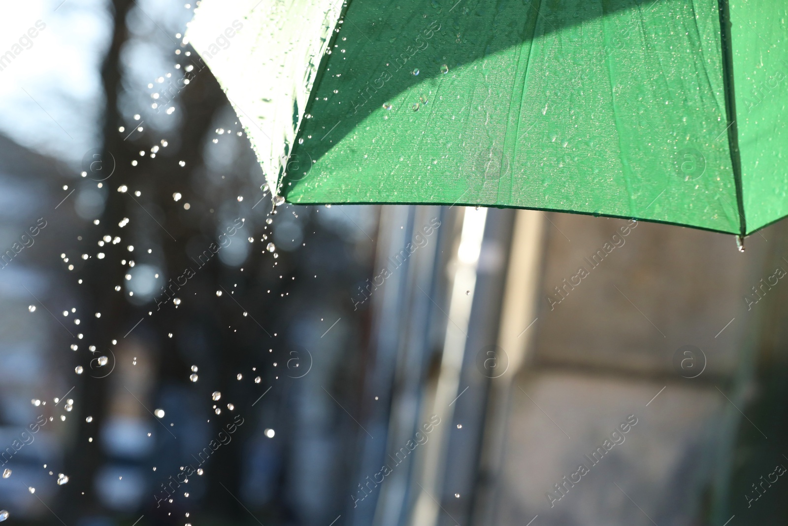 Photo of Open green umbrella under pouring rain outdoors, closeup