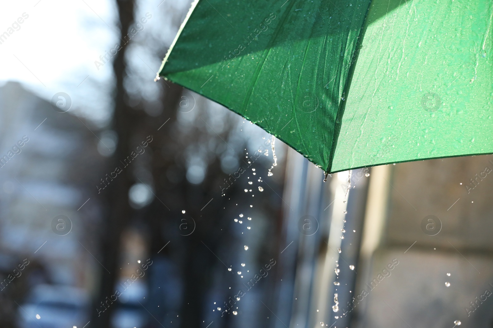 Photo of Open green umbrella under pouring rain outdoors, closeup