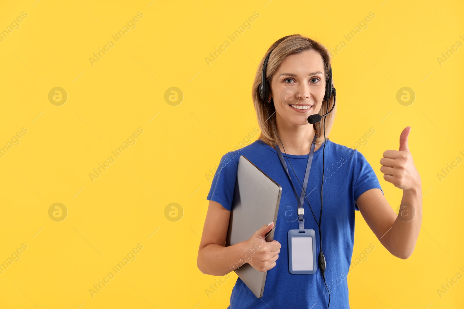 Photo of Technical support call center. Smiling operator with laptop showing thumbs up on yellow background. Space for text