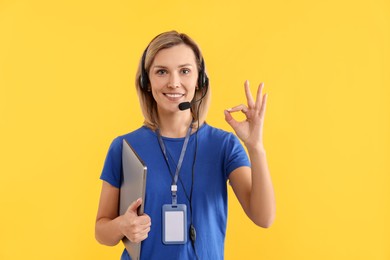 Photo of Technical support call center. Smiling operator with laptop showing ok gesture on yellow background