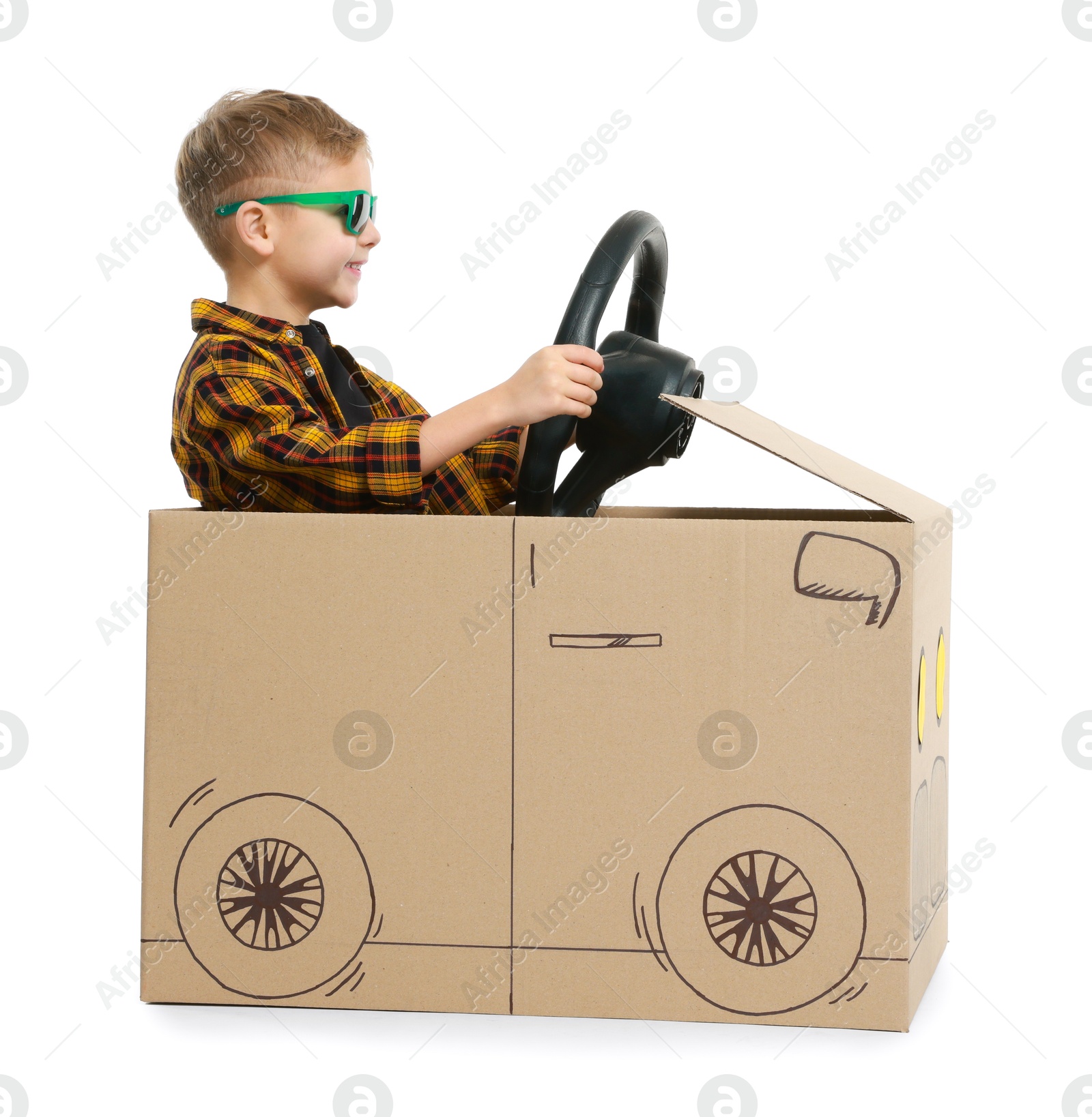 Photo of Little boy in sunglasses driving car made of cardboard on white background