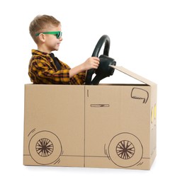 Photo of Little boy in sunglasses driving car made of cardboard on white background