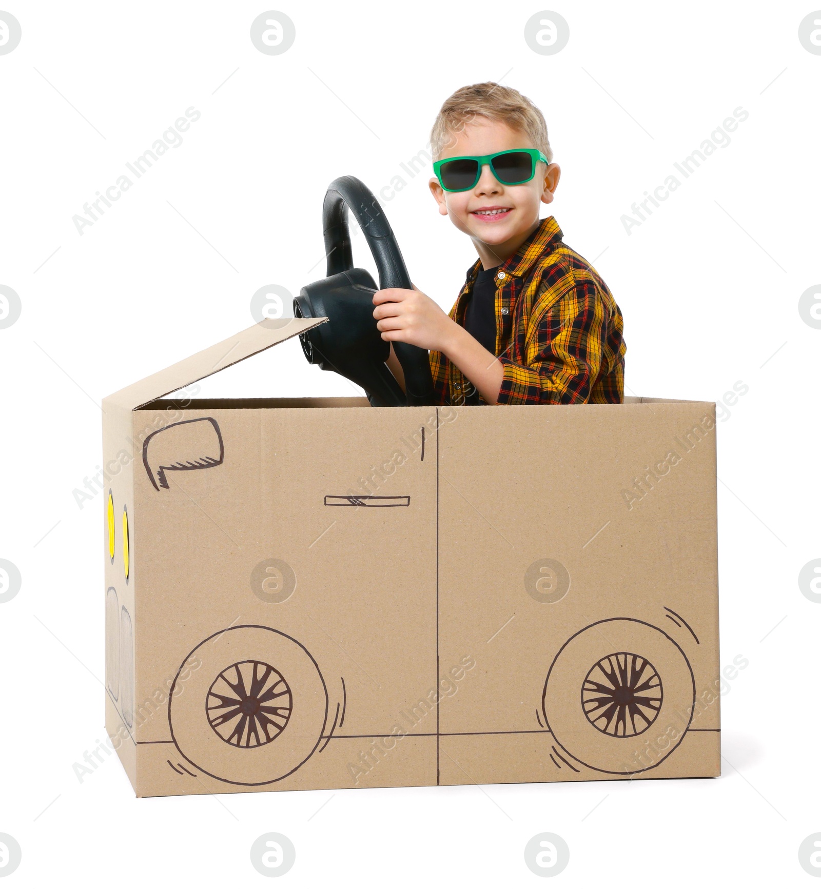 Photo of Little boy in sunglasses driving car made of cardboard on white background