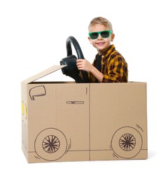 Photo of Little boy in sunglasses driving car made of cardboard on white background