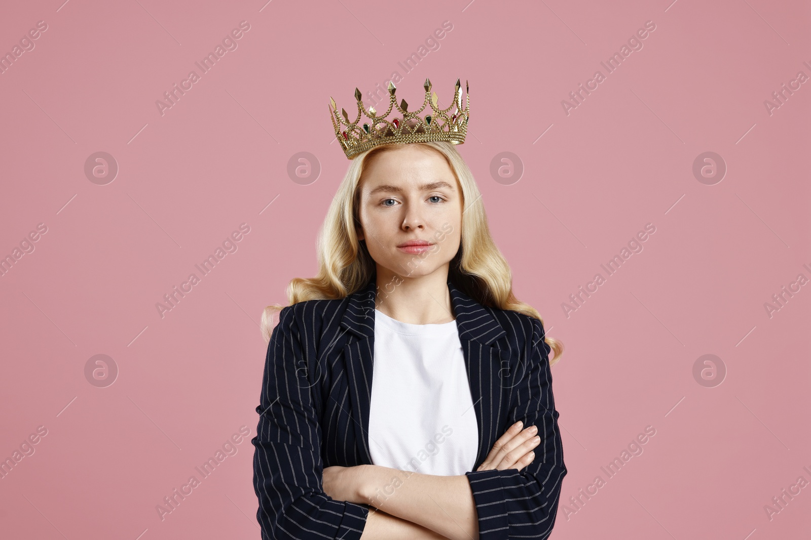 Photo of Businesswoman in elegant crown with crossed arms on dusty pink background