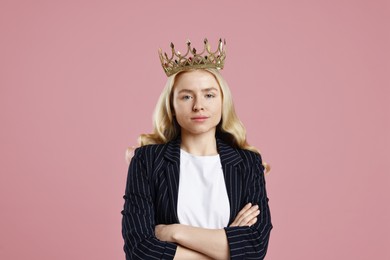 Businesswoman in elegant crown with crossed arms on dusty pink background