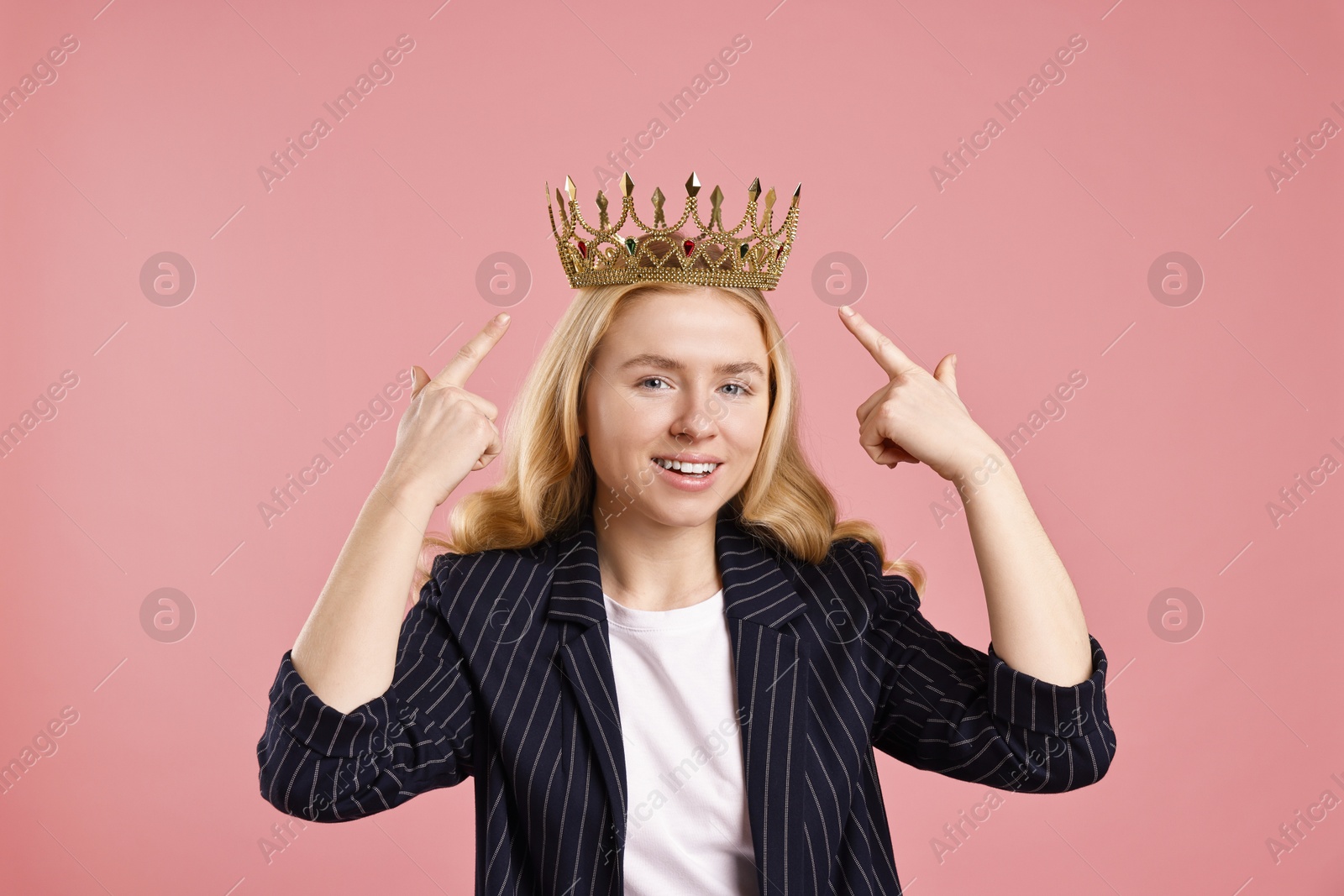 Photo of Smiling businesswoman pointing at elegant crown on dusty pink background