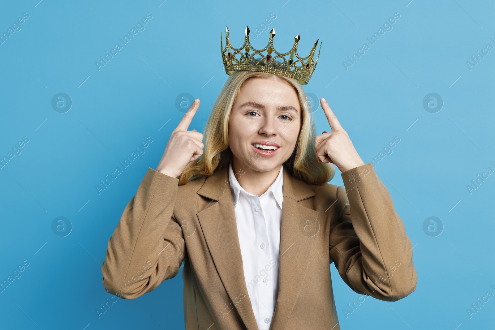 Photo of Smiling businesswoman pointing at elegant crown on light blue background