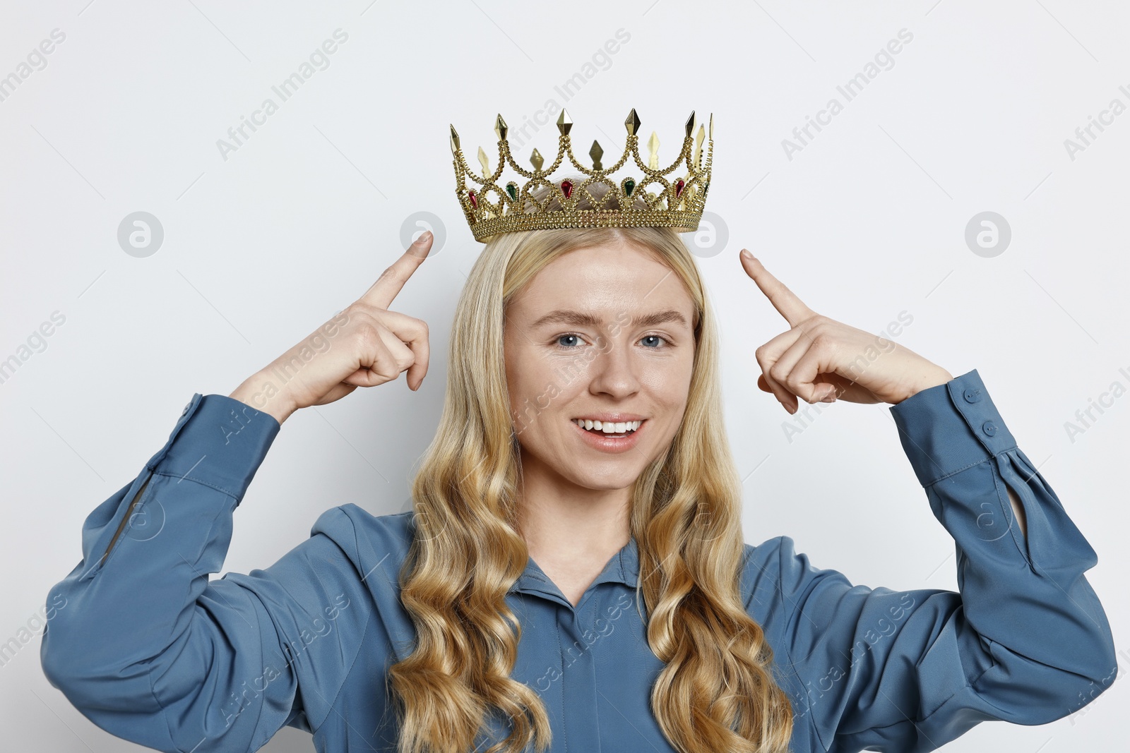 Photo of Smiling woman pointing at elegant crown on light background