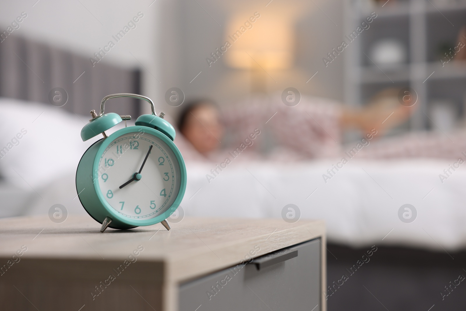 Photo of Young woman exercising on bed at home, focus on alarm clock. Morning routine