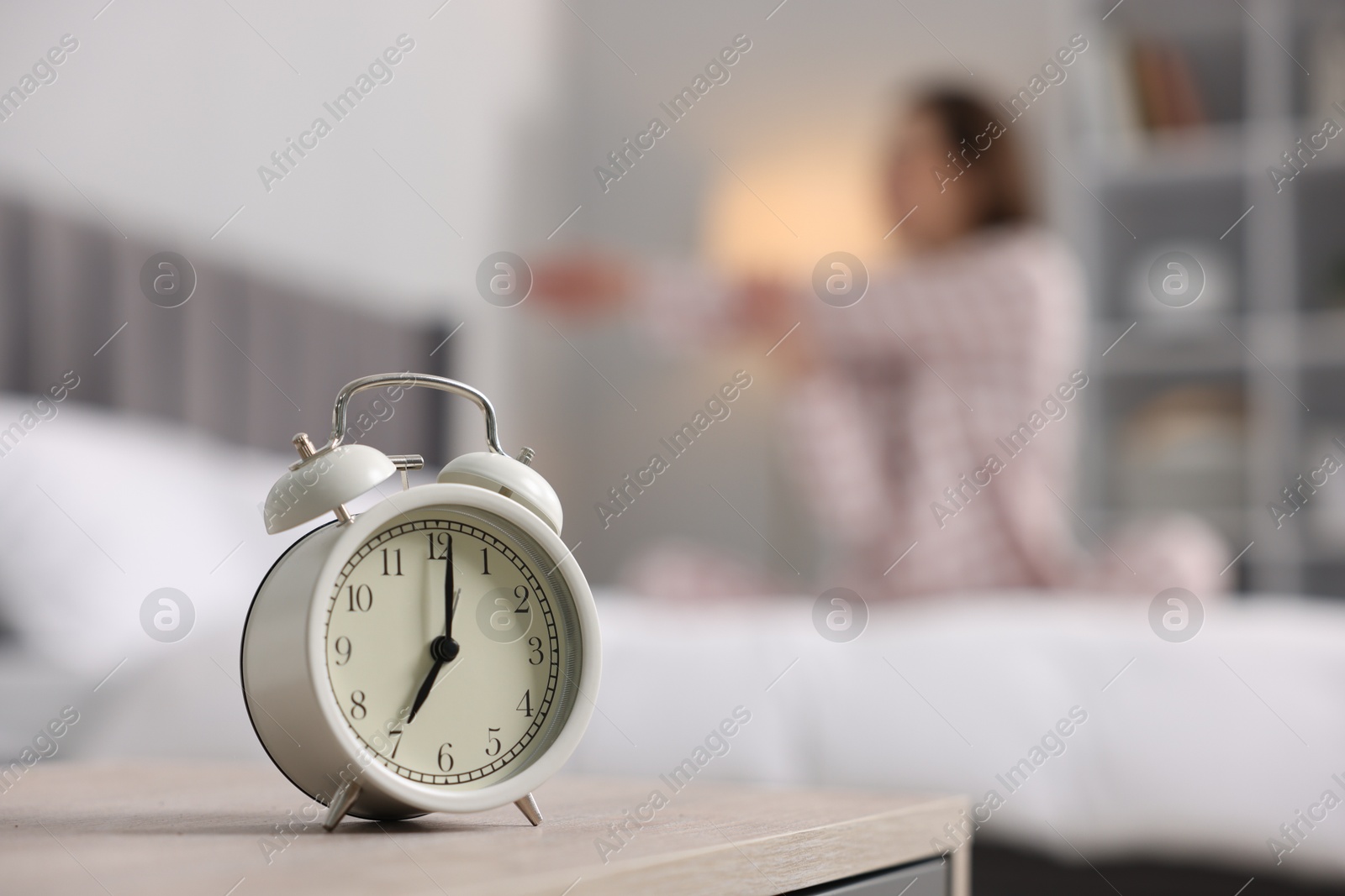 Photo of Young woman exercising on bed at home, focus on alarm clock. Morning routine