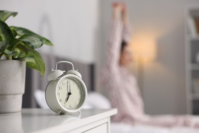 Photo of Young woman exercising on bed at home, focus on alarm clock. Morning routine