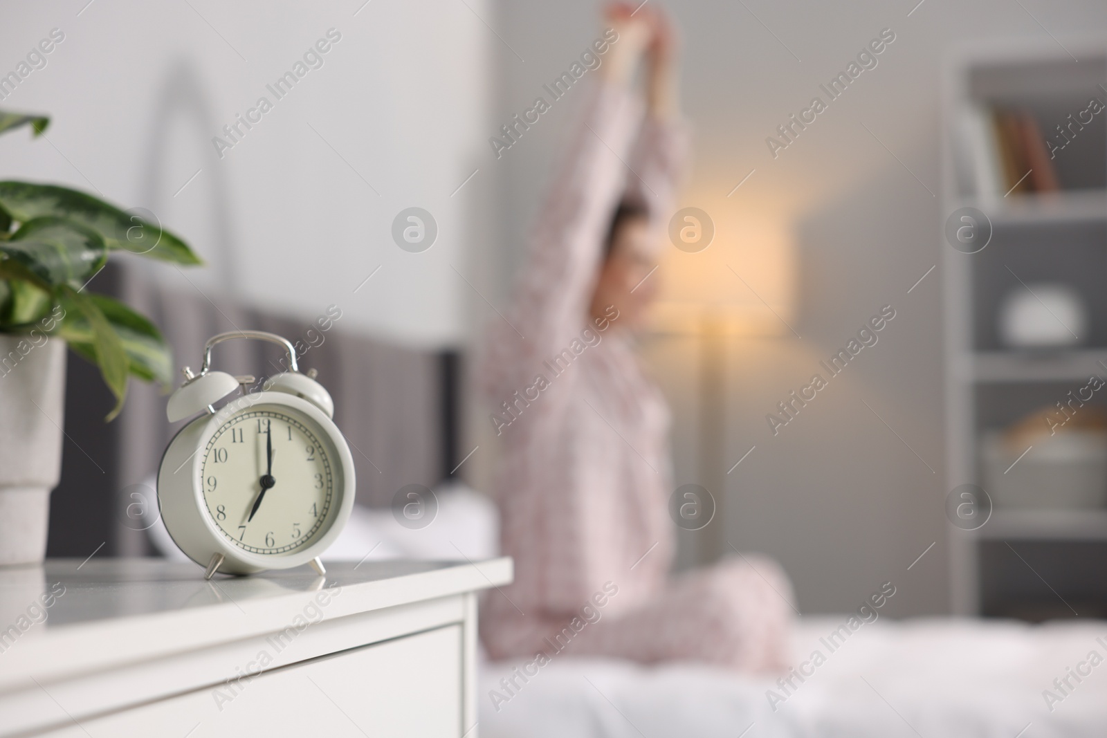 Photo of Young woman exercising on bed at home, focus on alarm clock. Morning routine