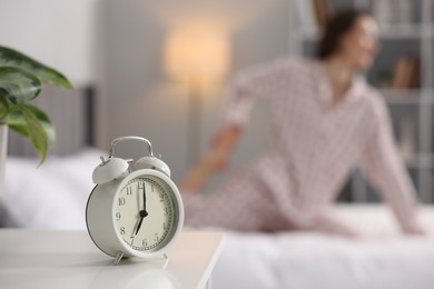 Young woman exercising on bed at home, focus on alarm clock. Morning routine