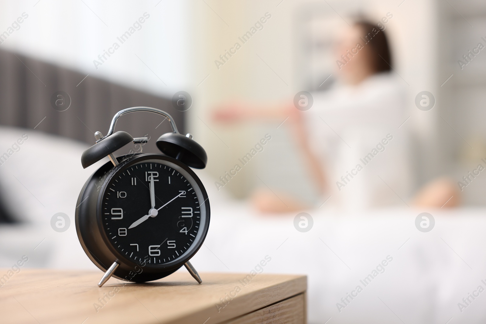 Photo of Young woman exercising on bed at home, focus on alarm clock. Morning routine