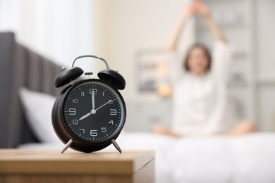 Photo of Young woman exercising on bed at home, focus on alarm clock. Morning routine