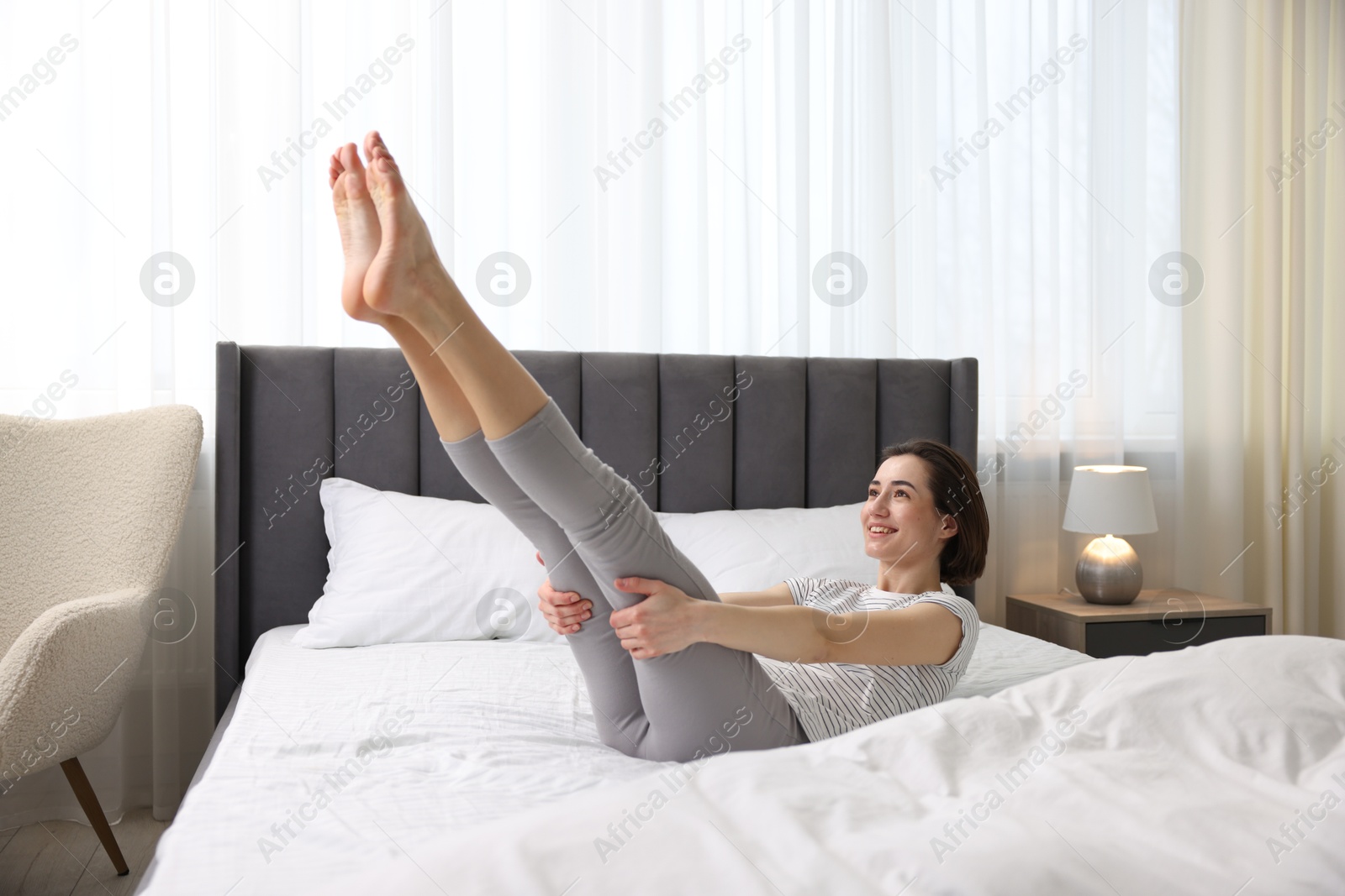 Photo of Young woman exercising on bed at home. Morning routine