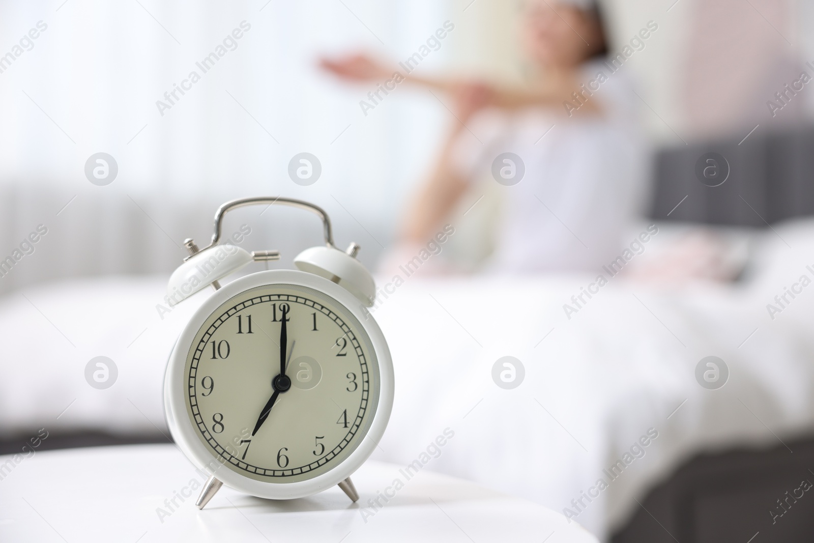 Photo of Young woman exercising on bed at home, focus on alarm clock. Morning routine