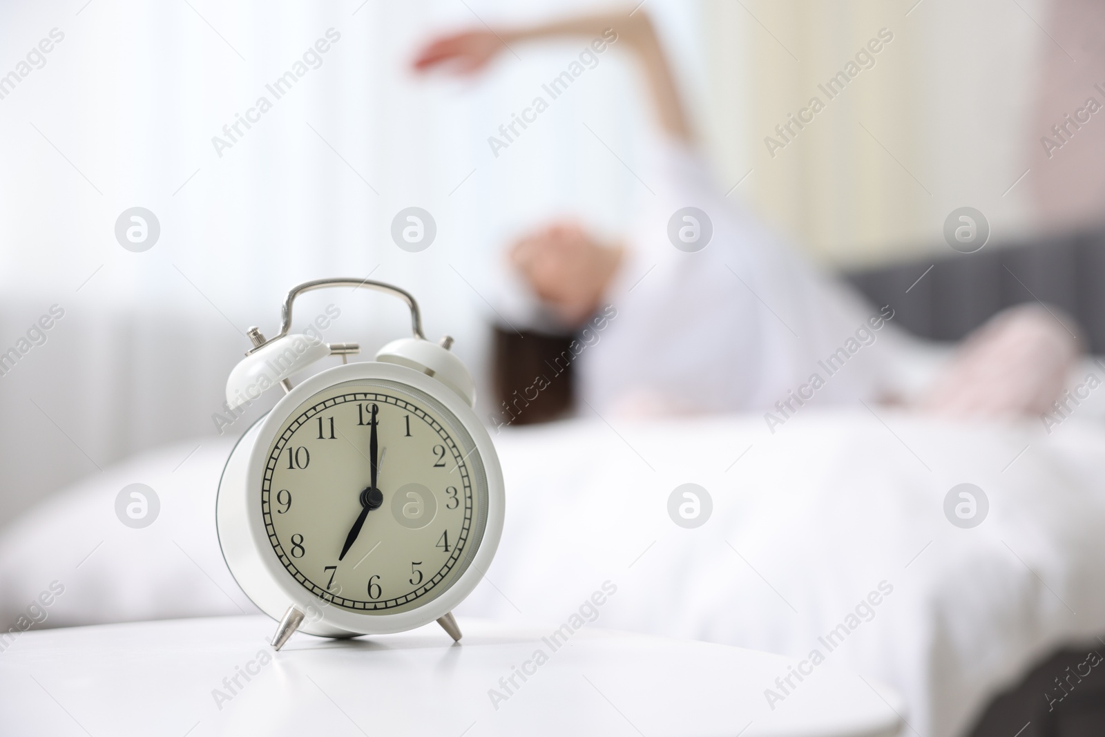 Photo of Young woman exercising on bed at home, focus on alarm clock. Morning routine