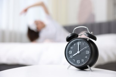 Photo of Young woman exercising on bed at home, focus on alarm clock. Morning routine