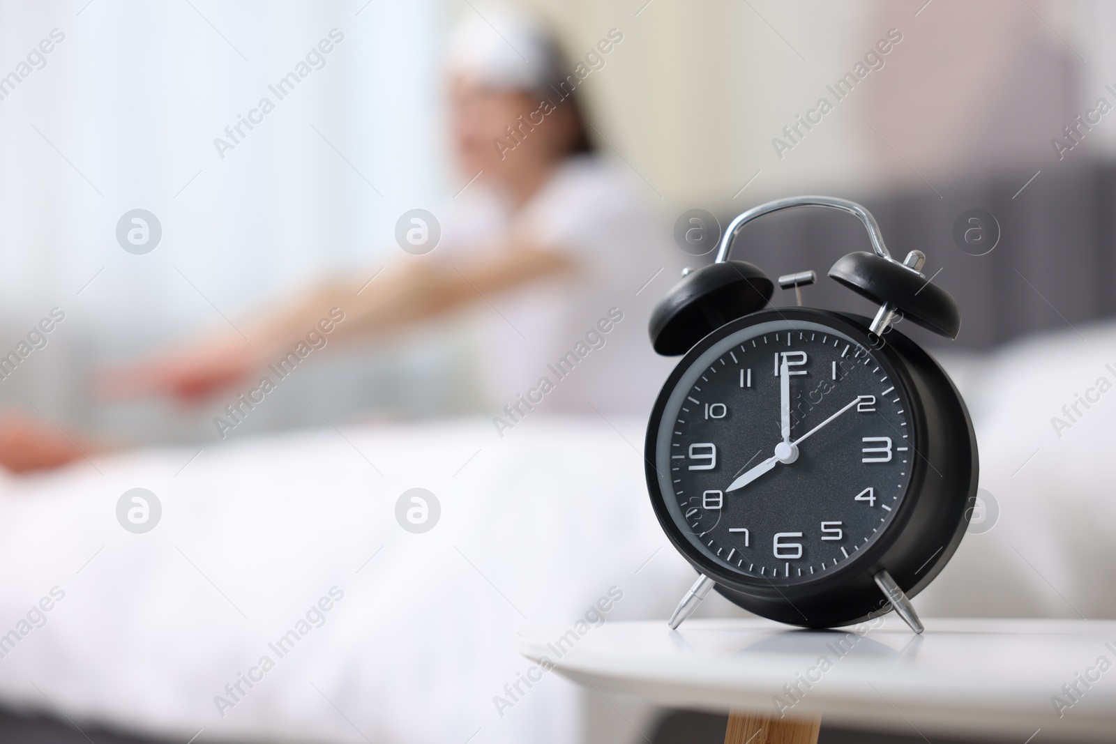 Photo of Young woman exercising on bed at home, focus on alarm clock. Morning routine