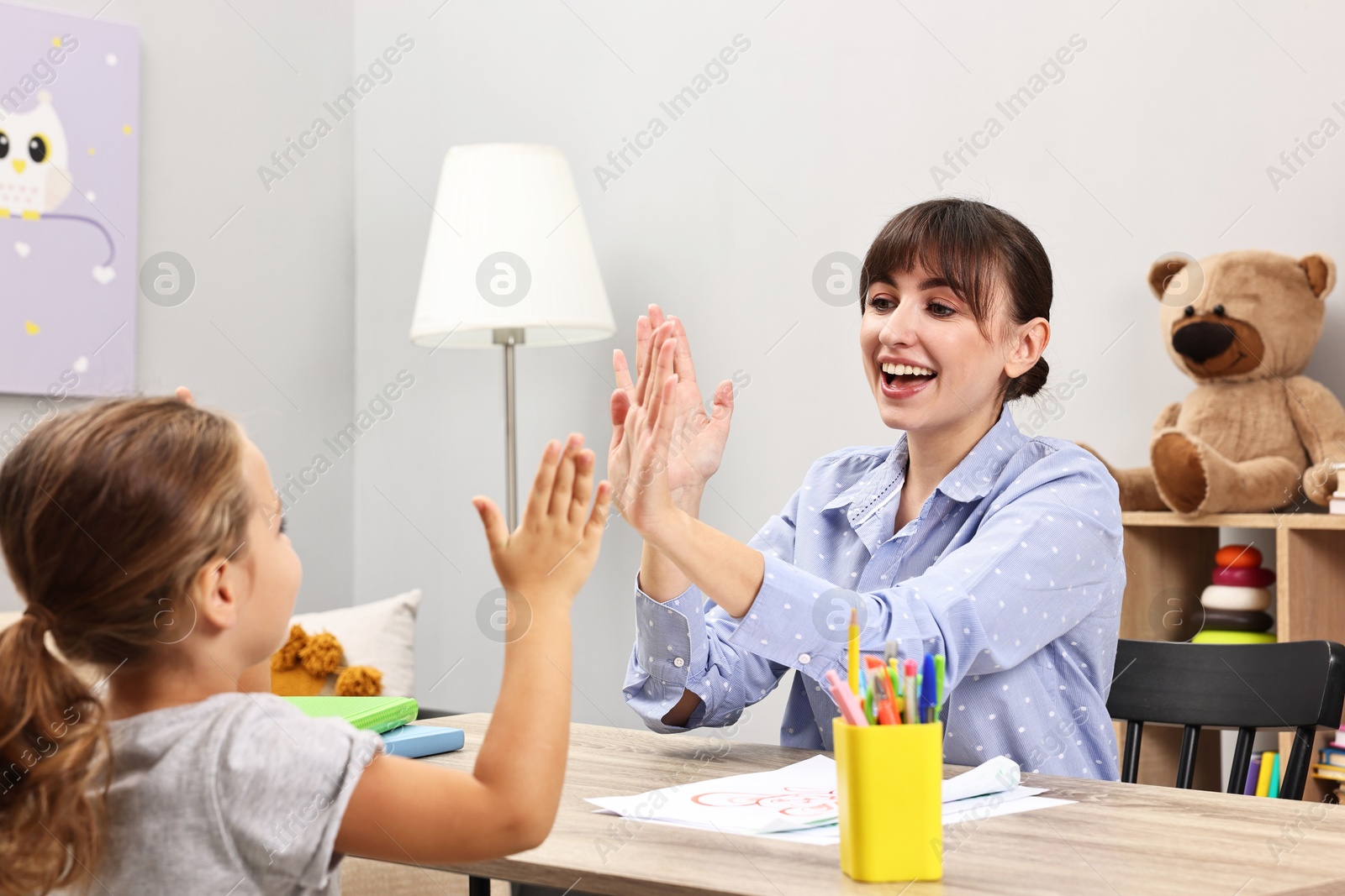 Photo of Autism therapy. Smiling psychologist playing with little girl at table in mental health center