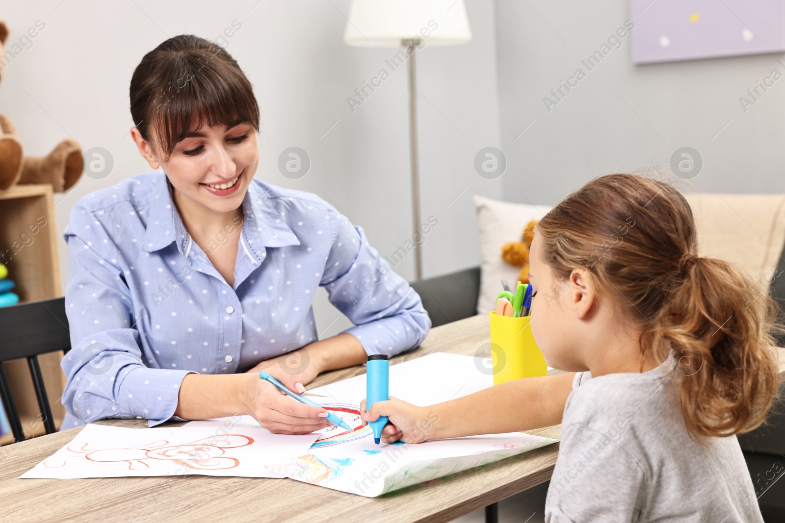 Photo of Autism therapy. Smiling psychologist and little girl drawing pictures at table in mental health center