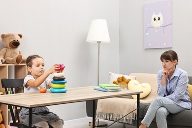 Therapist observing little girl playing in autism treatment center