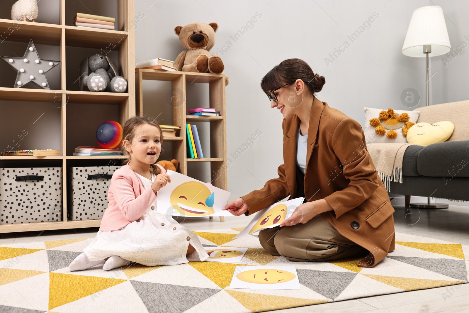 Photo of Autism therapy. Little girl choosing emoticon with smiling psychologist in mental health center