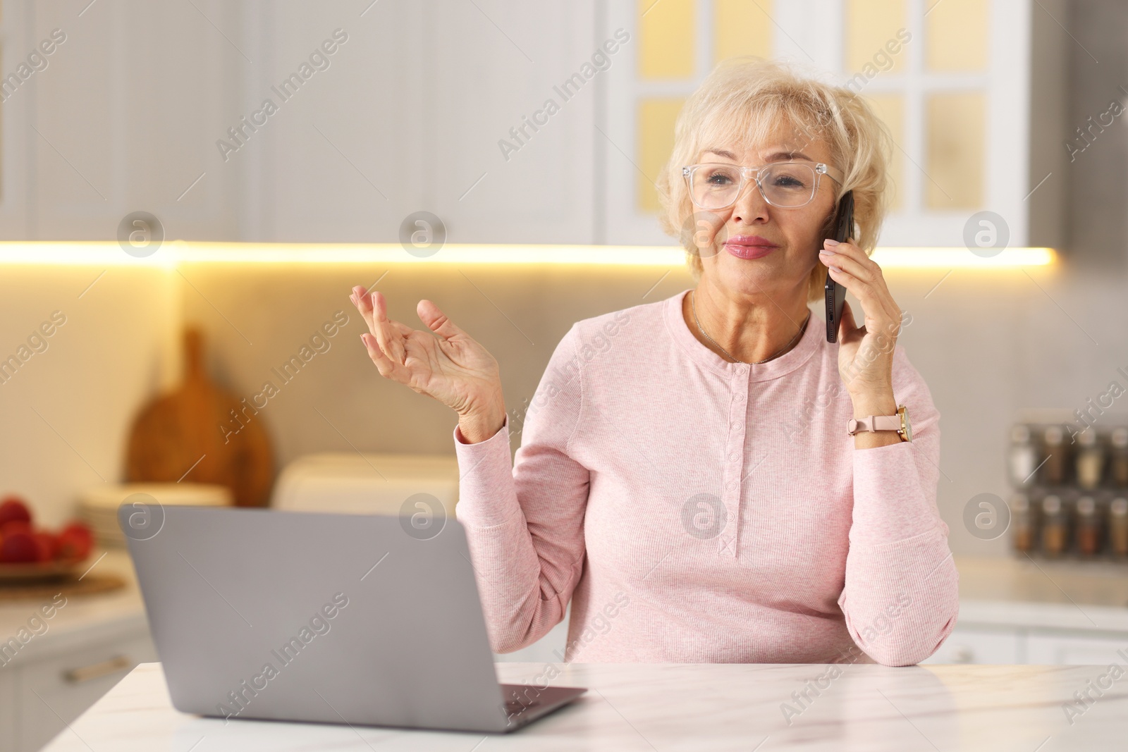 Photo of Beautiful grandmother talking on smartphone at table in kitchen