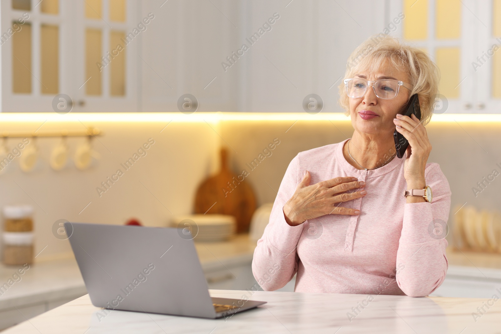 Photo of Beautiful grandmother talking on smartphone at table in kitchen