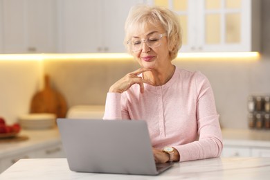 Photo of Beautiful grandmother using laptop at table in kitchen