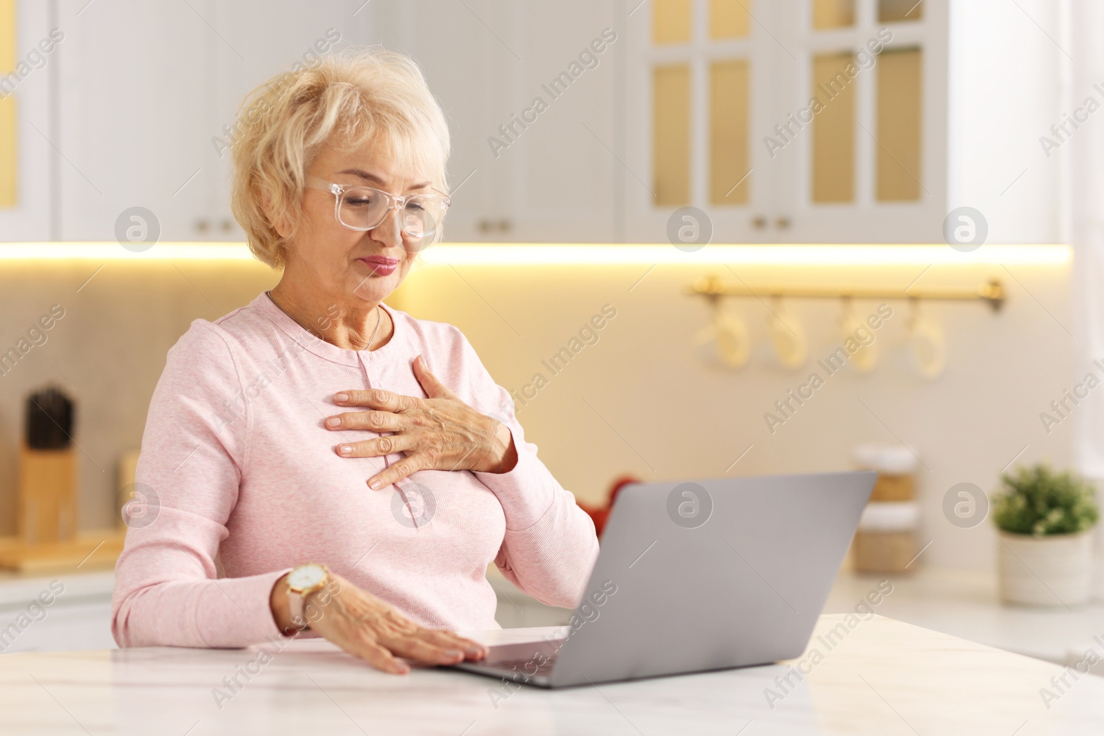 Photo of Beautiful grandmother using laptop at table in kitchen. Space for text